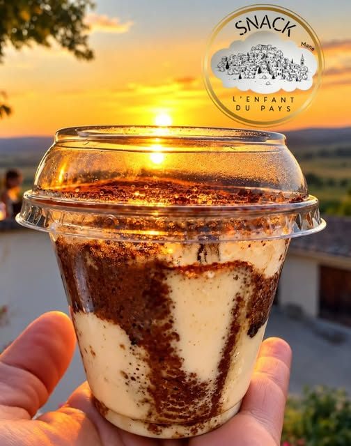Tiramisu maison tenu à la main devant un coucher de soleil
